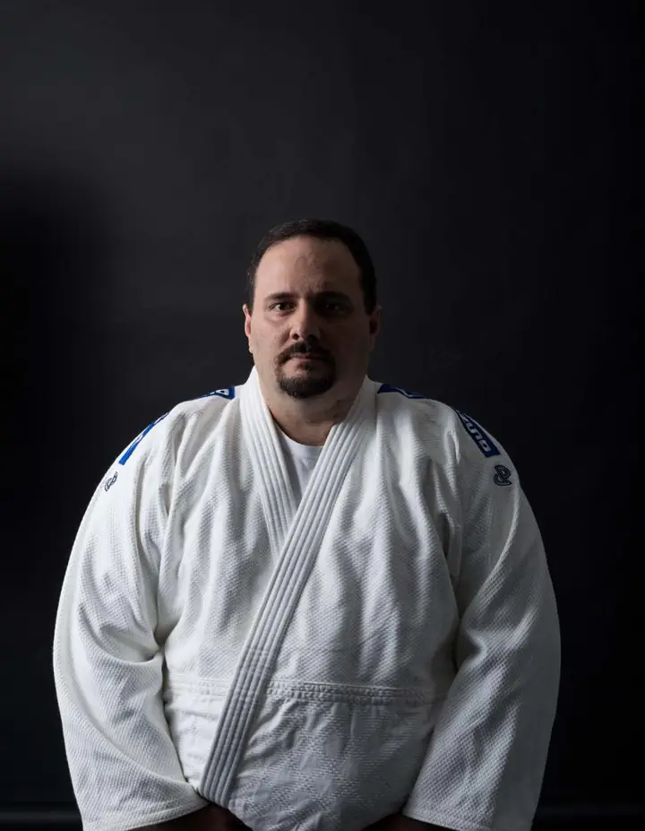 Retrato de Mestre Li, de quimono branco e faixa vermelha, em pé, diante de um fundo escuro.